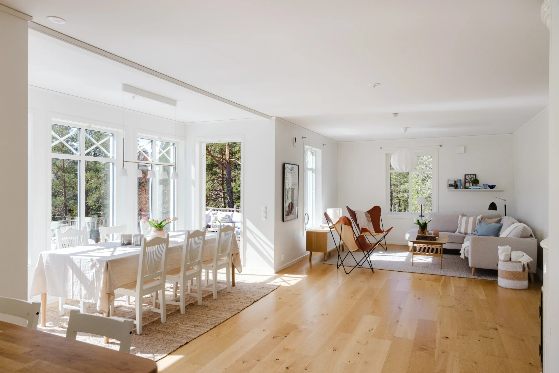 Séjour lumineux d’une maison suédoise, grande table et vue sur les pins