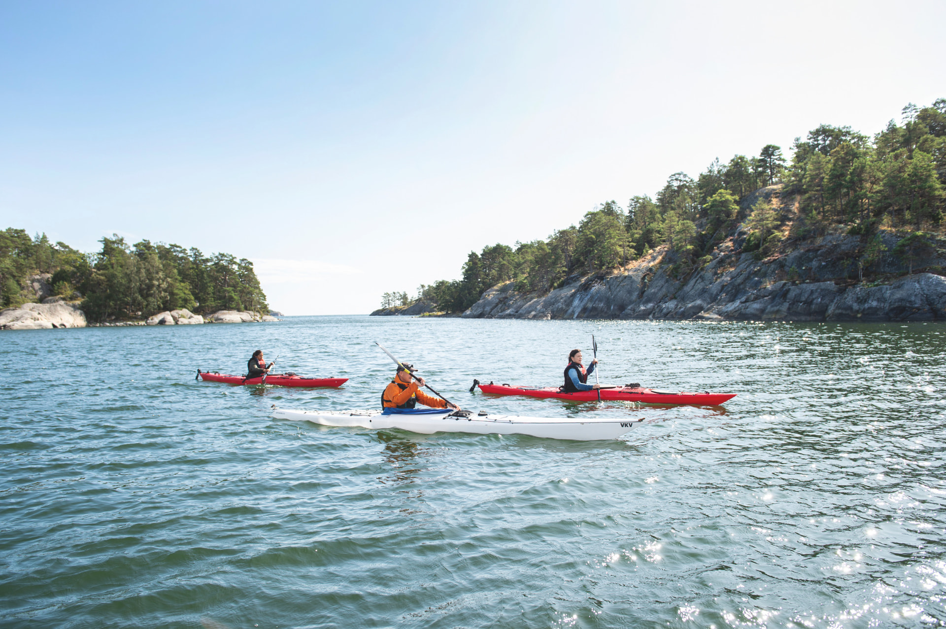 Trois kayaks sur l’eau calme de l’archipel de Stockholm, entre forêts et granite