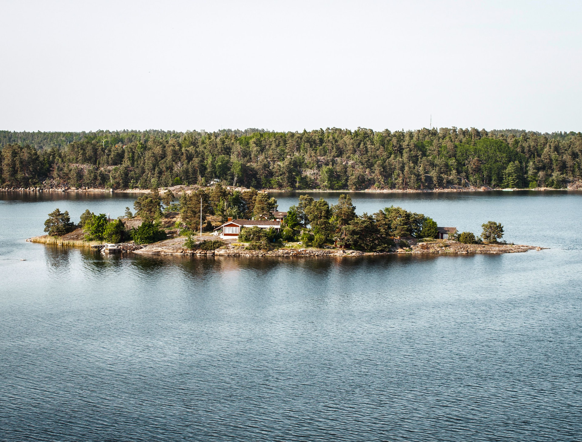 Petite île boisée avec une maison rouge, entourée d’eau calme dans l’archipel de Stockholm